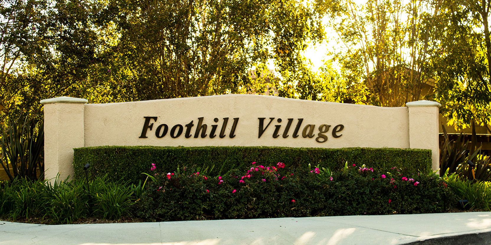 The Foothill Village entrance sign framed by trees and flowers